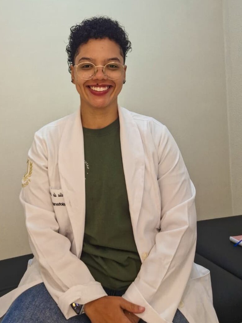 Nathalia de Oliveira, fisioterapeuta, de jaleco branco no consultório